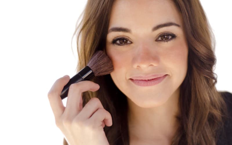 A caucasian woman is putting on blush