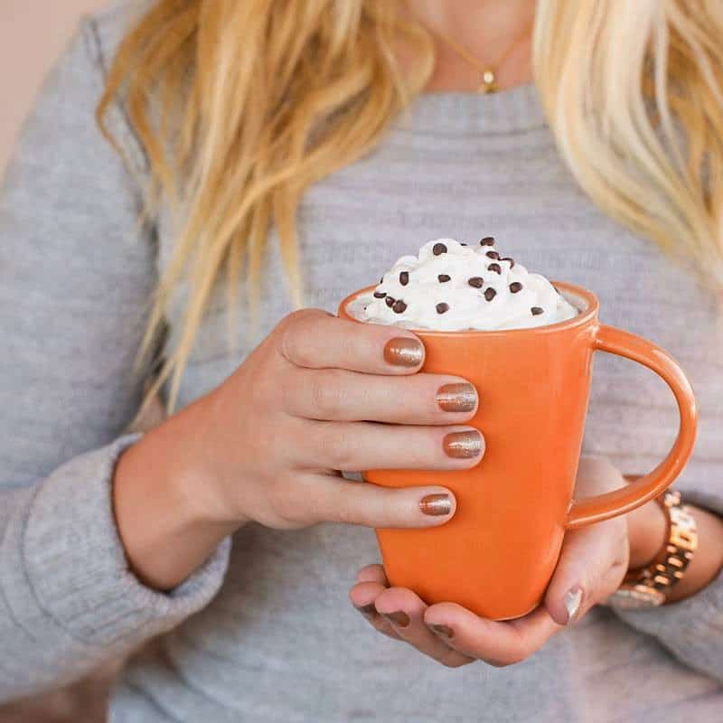 Woman with her nails painted is holding a pumpkin spice